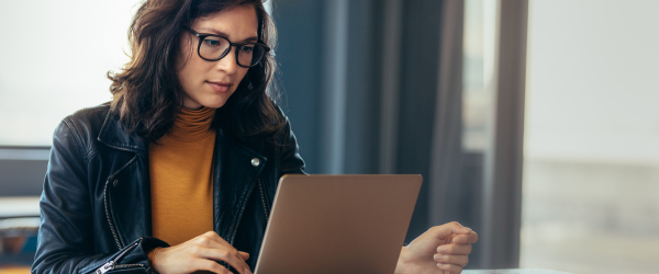 Woman wearing glasses working on a laptop at a desk in a modern office setting.